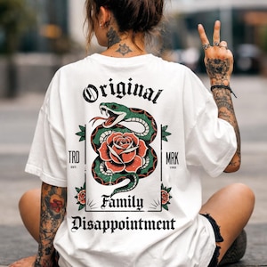 May include: White t-shirt with a graphic of a green snake and red rose. The text "Original Family Disappointment" is displayed above and below the graphic. Additional text includes "TRD EST." and "MRK 1993".