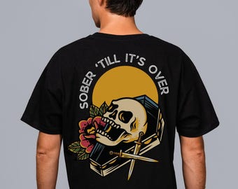 May include: Black t-shirt with a graphic print of a skull in a coffin with a rose and daggers. The text "SOBER 'TILL IT'S OVER" is printed in a circle around the skull.
