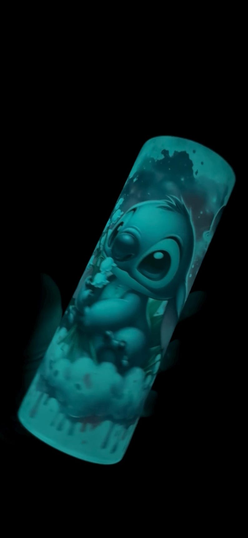 May include: A teal-colored tumbler featuring a cartoon illustration of Stitch from Lilo & Stitch. The design glows in the dark, showcasing Stitch's face and form against a cloudy background. The tumbler is cylindrical and appears to be made of plastic.