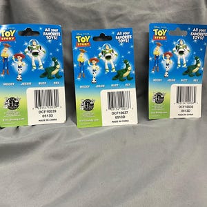 K&ouml;nnte beinhalten: Drei Sammelkarten mit Toy Story-Charakteren, die Woody, Jessie, Buzz Lightyear und Rex zeigen. Die Karten sind blau, gelb und rot mit dem Text "All your favorite toys!" und "Toy Story".