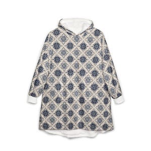 May include: A hooded blanket with a cream-colored background and a repeating blue geometric pattern. The hood and cuffs are white. The blanket is designed to be worn.
