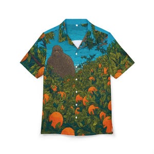 May include: Short-sleeved button-down shirt with a colorful illustration. The shirt features a brown Bigfoot figure in an orange grove with a blue sky background. The design includes orange fruit and green foliage.