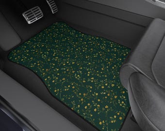 May include: A dark green car floor mat featuring a pattern of small yellow flowers and vines. The mat has a black border and is positioned in the driver's side footwell of a vehicle.