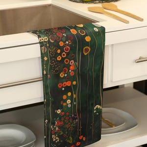 May include: A kitchen towel with a green background and a colorful floral pattern. The towel is hanging on a white cabinet door.