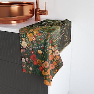 May include: A green and gold floral patterned kitchen towel with a dark green background. The towel is folded and draped over a countertop.