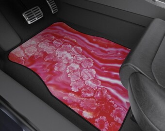 May include: A car floor mat with a vibrant red and white abstract design. The mat features a pattern of pink floral shapes and flowing lines, bordered by a black edge. The mat is placed in the driver's side footwell of a car.