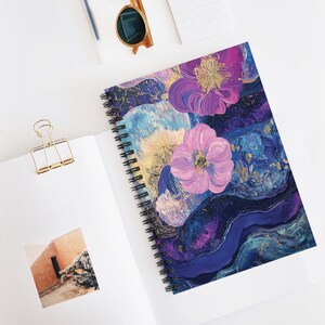 May include: Spiral-bound notebook with a vibrant floral design. The cover features a watercolor-style painting with purple, blue, and gold accents. Two large pink flowers are prominent, set against an abstract background.