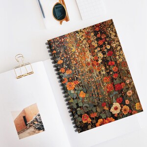 May include: Spiral-bound notebook featuring a floral design with red, orange, and yellow flowers. The cover has a dark background with a field of flowers. The notebook is open on a white surface with a gold paper clip and sunglasses.
