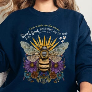 May include: Navy blue sweatshirt with a bee and floral design. The text "Sweet Soul to the" and "Kind words are like honey and healthy for the body!" is printed on the sweatshirt. The Bible verse "Proverbs 16:24" is also printed on the sweatshirt.