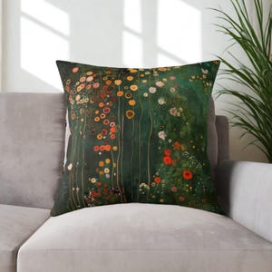 May include: A decorative throw pillow featuring a floral design in shades of green, orange, red, and yellow. The pillow is square and rests on a gray sofa, with a plant in the background.