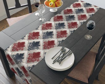 Puede incluir: Una mesa de comedor de madera oscura con un camino de mesa estampado, platos blancos y copas de vino. El camino de mesa presenta un patrón repetido de diseños de hojas rojas y azul marino sobre un fondo crema. Un cuenco de manzanas está sobre la mesa.