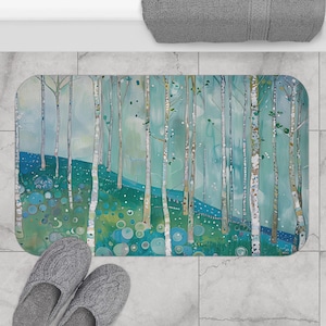 May include: Rectangular bath mat featuring an artistic forest scene with tall, slender trees and a grassy foreground. The color palette includes shades of blue, green, and white. Gray slippers are placed near the mat.