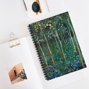 May include: Spiral-bound notebook with a vibrant, abstract forest design in shades of green, blue, and gold. The cover features a repeating pattern of circles and lines, creating a textured appearance. The notebook is open on a white surface.