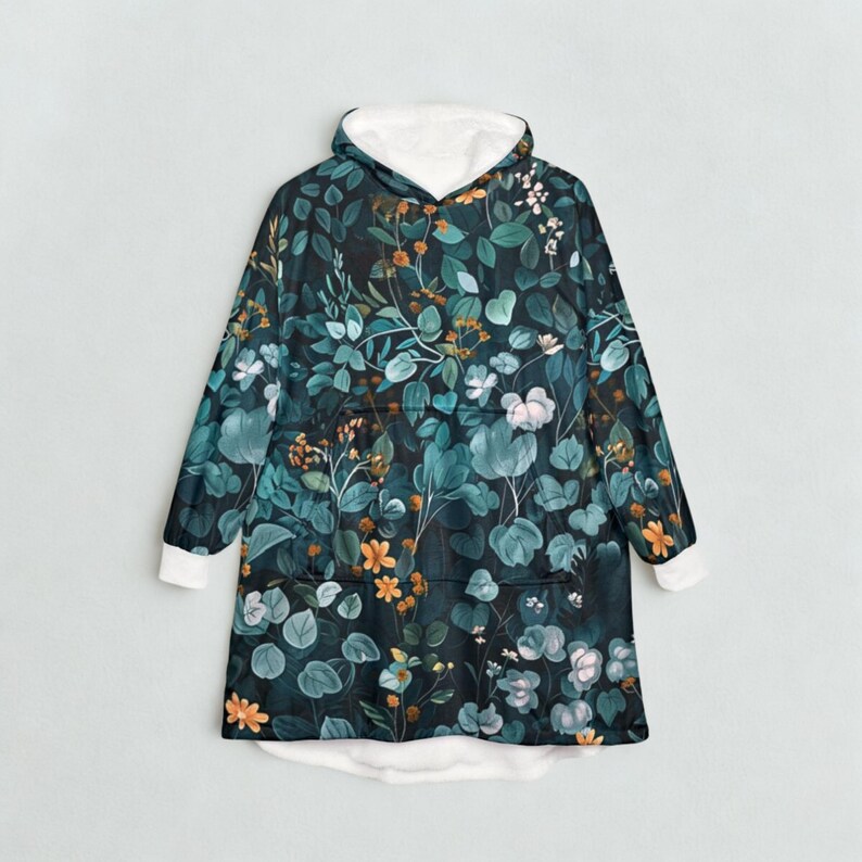 K&ouml;nnte beinhalten: Eine Kapuzen-Decke mit botanischem Druck mit teal-, gr&uuml;nen und orangefarbenen Blumen- und Blattelementen. Der Innenraum und die Manschetten sind wei&szlig;. Die Decke hat eine gro&szlig;e Fronttasche und eine gem&uuml;tliche, &uuml;bergro&szlig;e Passform.