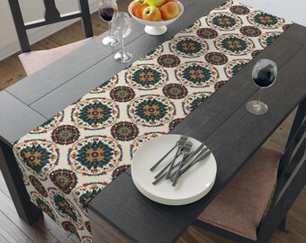 May include: A dining table set for a meal, featuring a patterned table runner with teal, orange, and cream circular designs. The table is set with white plates, silverware, wine glasses, and a bowl of apples. The table and chairs are dark wood.