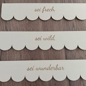 May include: Three wooden signs with scalloped edges and the text "sei frech", "sei wild", and "sei wunderbar" in a cursive font.