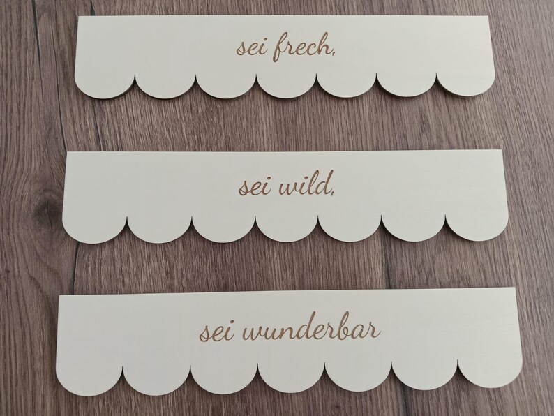 May include: Three wooden signs with scalloped edges and the text "sei frech", "sei wild", and "sei wunderbar" in a cursive font.