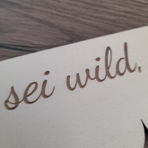 May include: A white wooden sign with a scalloped edge and the text "sei wild" written in cursive.