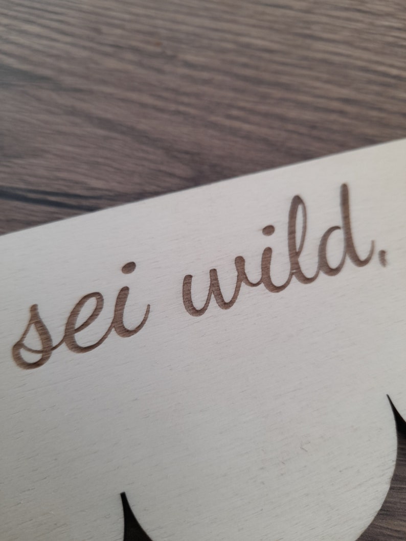 May include: A white wooden sign with a scalloped edge and the text "sei wild" written in cursive.