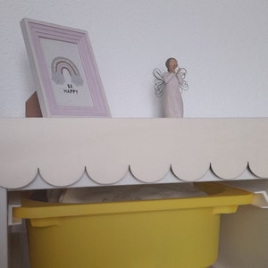 May include: A white shelf with a scalloped edge, a yellow storage bin, and a framed print with a rainbow and the words "Be Happy".