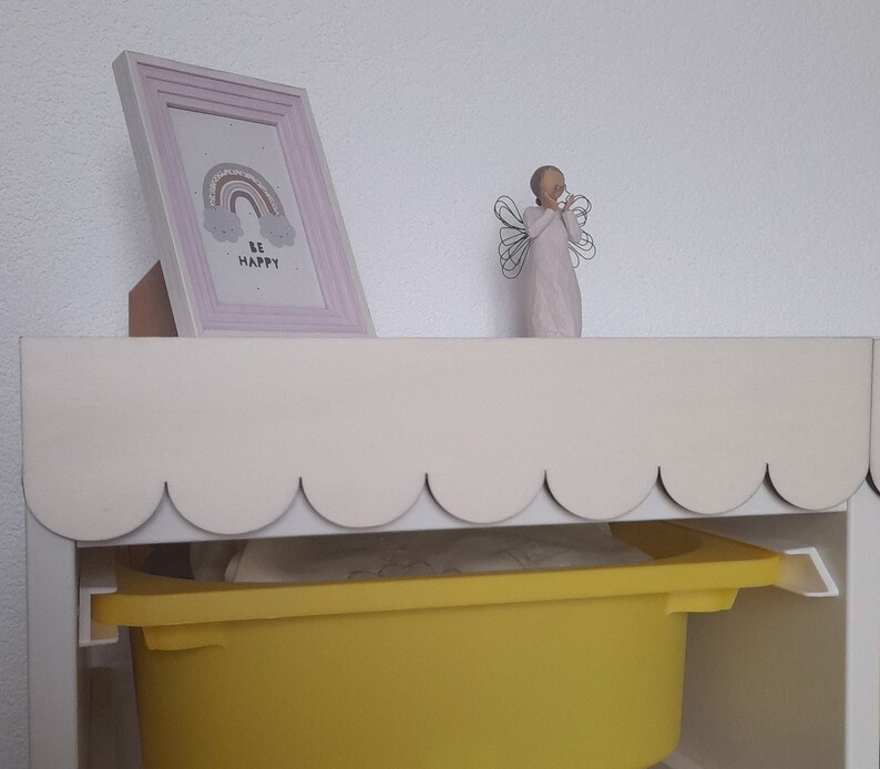 May include: A white shelf with a scalloped edge, a yellow storage bin, and a framed print with a rainbow and the words "Be Happy".