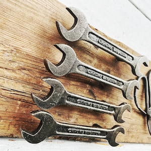 May include: Four vintage chrome wrenches with the text "Chrome Vanadium" on each, arranged on a wooden surface. A pair of vintage scissors is also on the surface.