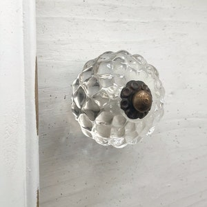 May include: A clear glass cabinet knob with a textured surface and a brass accent.