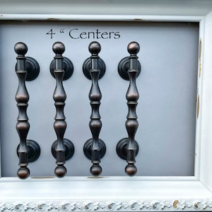 May include: Four antique bronze cabinet pulls with 4" centers. The pulls have a rounded top and a decorative, fluted design.