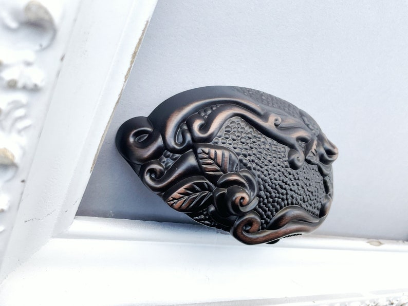 May include: A decorative cabinet pull with a floral design. The pull is made of metal and has a dark bronze finish.