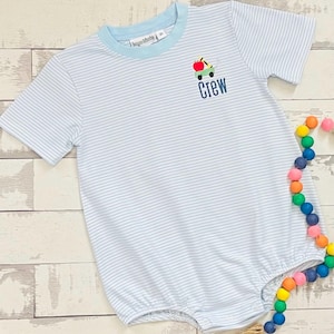 May include: A light blue and white striped romper with short sleeves and a light blue collar. The romper features an embroidered design of an apple and a car, with the word "Crew" below. The garment is made of a soft fabric.