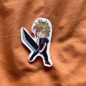 May include: A sticker featuring a cartoon illustration of a character with spiky blond hair holding a large sword. The character is wearing a blue shirt and black pants. The background is a light orange.