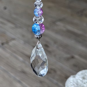 May include: A crystal suncatcher with a teardrop-shaped crystal hanging from a silver wire. The wire is strung with clear, blue, and pink glass beads.