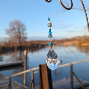 May include: A crystal teardrop suncatcher with a string of blue and white beads hanging from a copper wire.