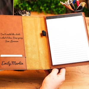 May include: A brown leather journal with a quote by Sam Levenson: "Don't watch the clock; do what it does. Keep going." The journal has a personalized name, "Emily Marlin", on the front cover.