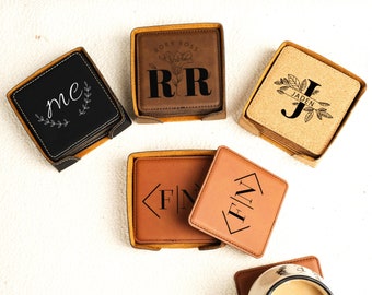May include: Set of six leather coasters with personalized initials and floral designs. The coasters are brown and black and come in a square shape. The coasters are arranged on a white surface.