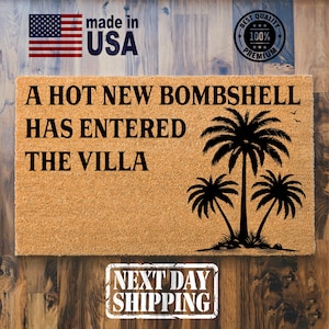 May include: A rectangular tan coir doormat featuring the black text A HOT NEW BOMBSHELL HAS ENTERED THE VILLA and a black graphic of three palm trees. The design includes a Made in USA flag icon and a Best Premium 100% quality circular seal.