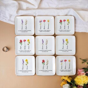Pu&ograve; includere: Nove porta anelli in ceramica bianca con bordo dorato e disegni floreali. Ogni porta anelli presenta un diverso arrangiamento floreale e un messaggio personalizzato. I messaggi includono nomi e citazioni sull'amicizia.
