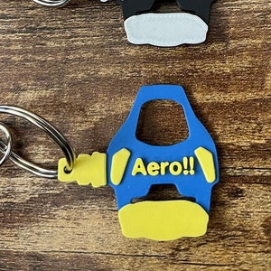 May include: Three keychains with car-shaped designs. One is yellow with "2Fast" in black, another is black with "Josh" in white, and the third is blue with "Aero!!" in yellow. Each keychain has a silver ring and clasp.