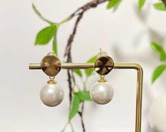 May include: A pair of gold earrings with a round pearl drop. The earrings have a textured gold disc above the pearl.