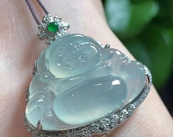 May include: A translucent, pale green carved jade pendant in the shape of a smiling Buddha figure. The pendant is set in a silver-toned metal frame accented with small, clear stones and features a small green stone at the top bail.
