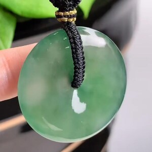 Pu&ograve; includere: Un ciondolo di giada verde a forma di cerchio con un foro al centro. Il ciondolo &egrave; appeso a un cordoncino nero con una chiusura dorata.