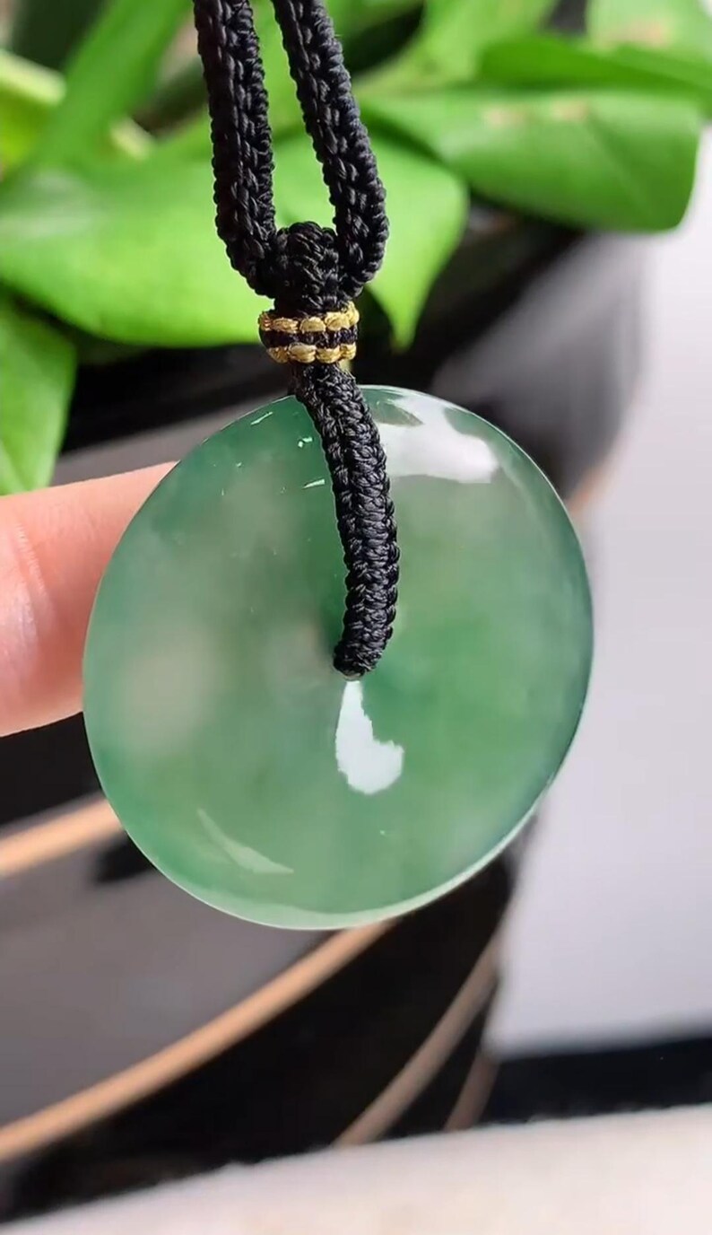 Pu&ograve; includere: Un ciondolo di giada verde a forma di cerchio con un foro al centro. Il ciondolo &egrave; appeso a un cordoncino nero con una chiusura dorata.