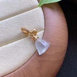 May include: A gold pendant featuring a translucent, pale lavender-grey stone shaped like a bell or flower bud. The gold bail is accented with small, clear stones and connects to a gold cap that secures the smooth, polished stone at the top.