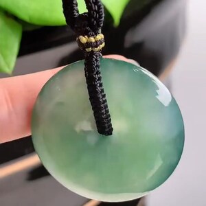 Pu&ograve; includere: Un ciondolo di giada verde su una collana di cordoncino nero. Il ciondolo &egrave; rotondo e ha una superficie liscia e lucida.