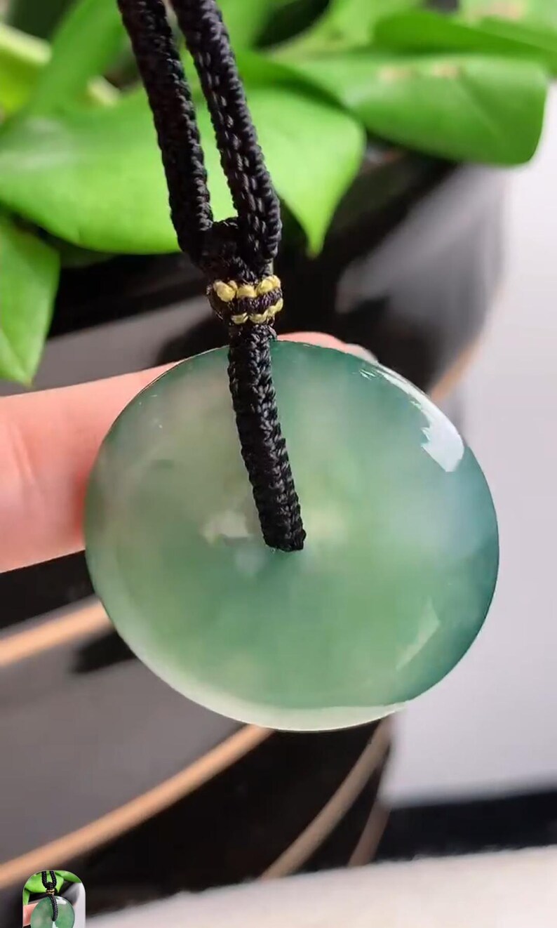 Pu&ograve; includere: Un ciondolo di giada verde su una collana di cordoncino nero. Il ciondolo &egrave; rotondo e ha una superficie liscia e lucida.