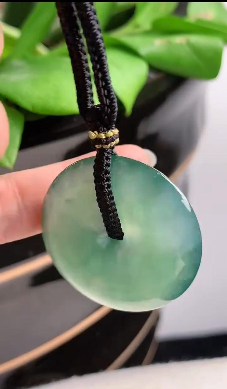 Pu&ograve; includere: Un ciondolo di giada verde a forma di cerchio con un cordoncino nero attaccato. Il ciondolo &egrave; appeso a un cordoncino nero.