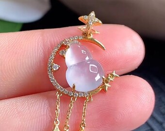 May include: A gold pendant featuring a translucent, pale purple, gourd-shaped stone set within a crescent moon frame encrusted with small clear stones. The design includes a star at the top and three dangling gold chains ending in star charms.