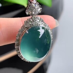 May include: A jade pendant necklace with a round, green jade stone set in a silver frame with a border of small diamonds.