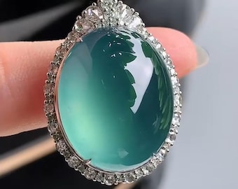 May include: A jade pendant with a green oval stone surrounded by a halo of small diamonds. The pendant is attached to a black cord.
