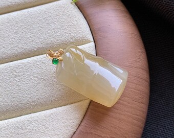 May include: A rectangular, translucent pale yellow jade pendant with a smooth, polished surface. The pendant features a gold-toned bail adorned with small clear stones and a single, small, round, vibrant green gemstone accent at the top.